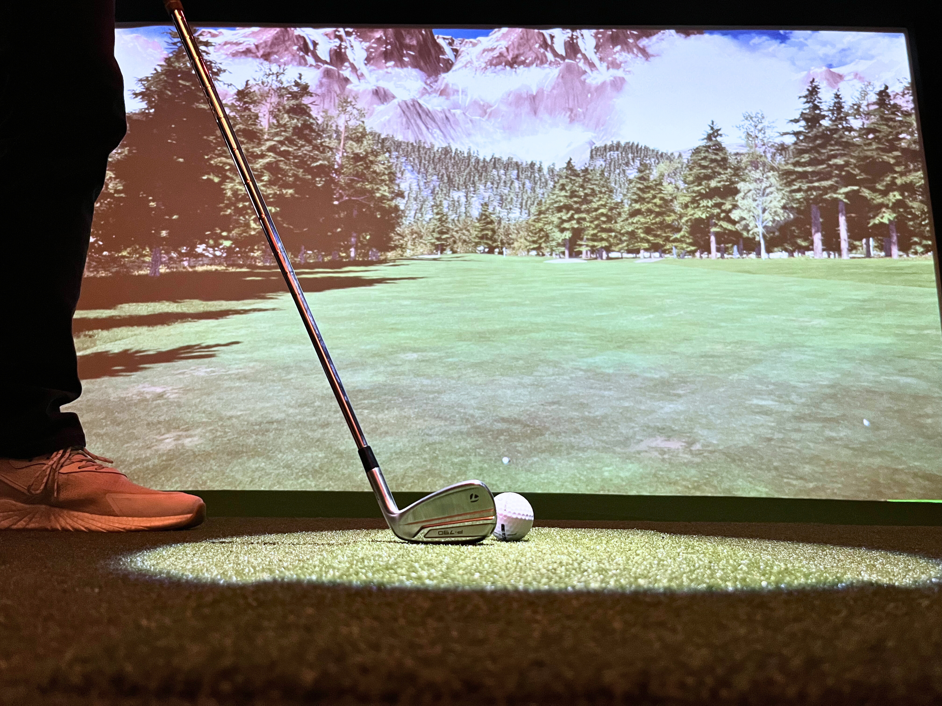 A modern golf simulator setup with a large screen, golf clubs, and a player swinging in a well-lit indoor space.