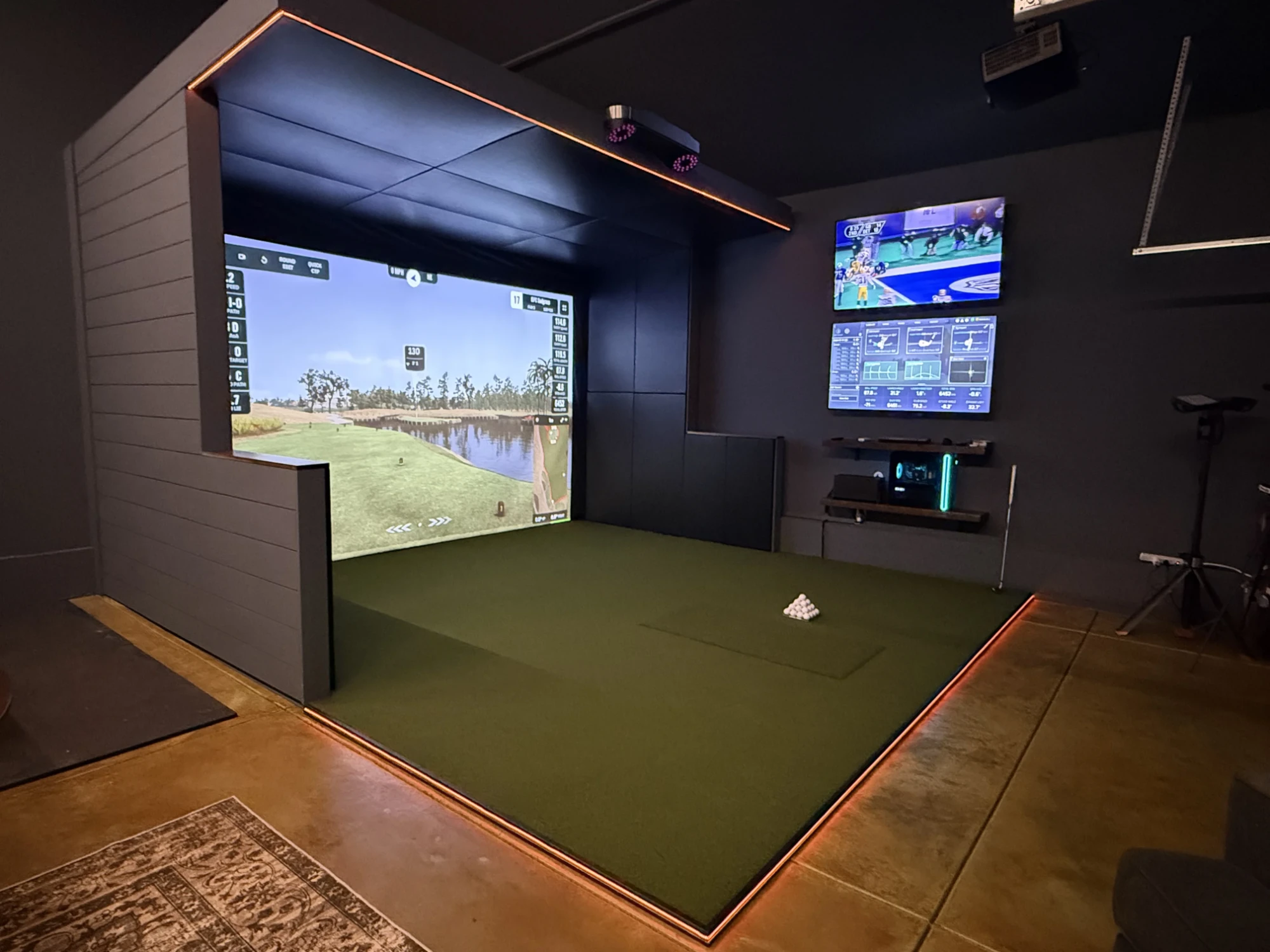 Finished simulator with orange LED strip along the cantilever edge and floor pad perimeter, running on a virtual golf course