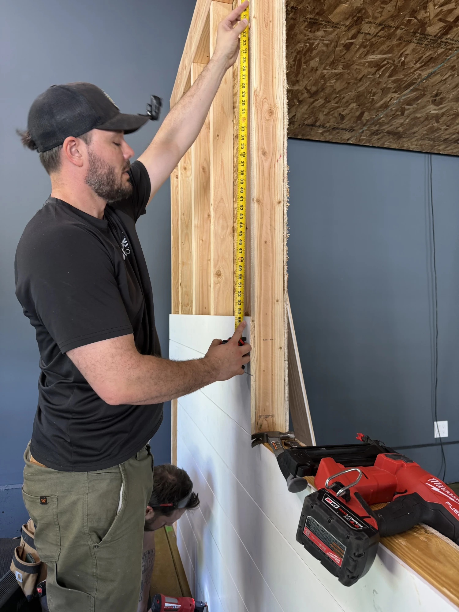 Installer measuring nickel-gap shiplap panels being installed on the enclosure wall